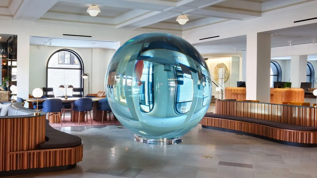 The lobby of 21c Museum Hotel St. Louis featuring a massive blue glass sphere sculpture and curved wood seating
