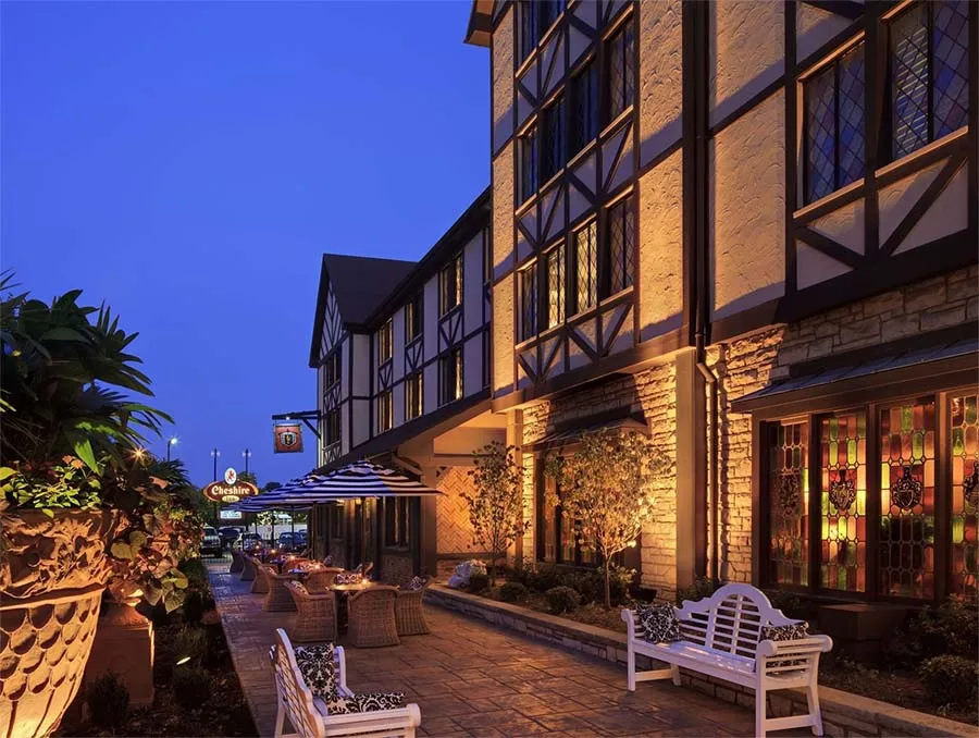 The Cheshire hotel exterior at dusk, showing the Tudor-style facade, outdoor patio, and stained glass windows in Richmond Heights, Missouri