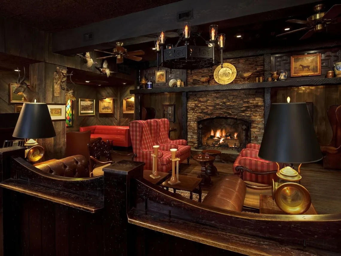 The Fox and Hounds bar at The Cheshire hotel, a hunting lodge style room with stone fireplace, leather chairs, and dark wood paneling