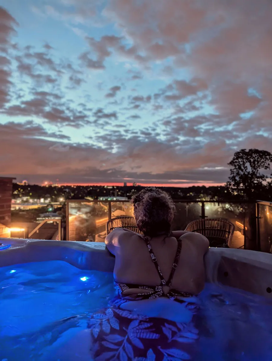 Guest relaxing in the rooftop hot tub at Gothic Heights Inn with the St. Louis skyline at sunset