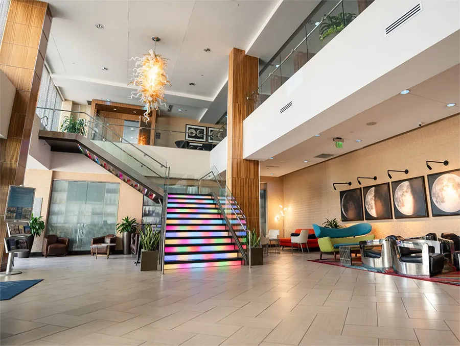 The Moonrise Hotel lobby featuring a rainbow-lit staircase, Chihuly glass chandelier, moon phase artwork, and retro-modern lounge seating