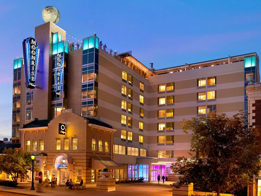 The Moonrise Hotel exterior at night on the Delmar Loop in St. Louis, showing the illuminated neon sign, rooftop bar, and the giant moon sculpture on top